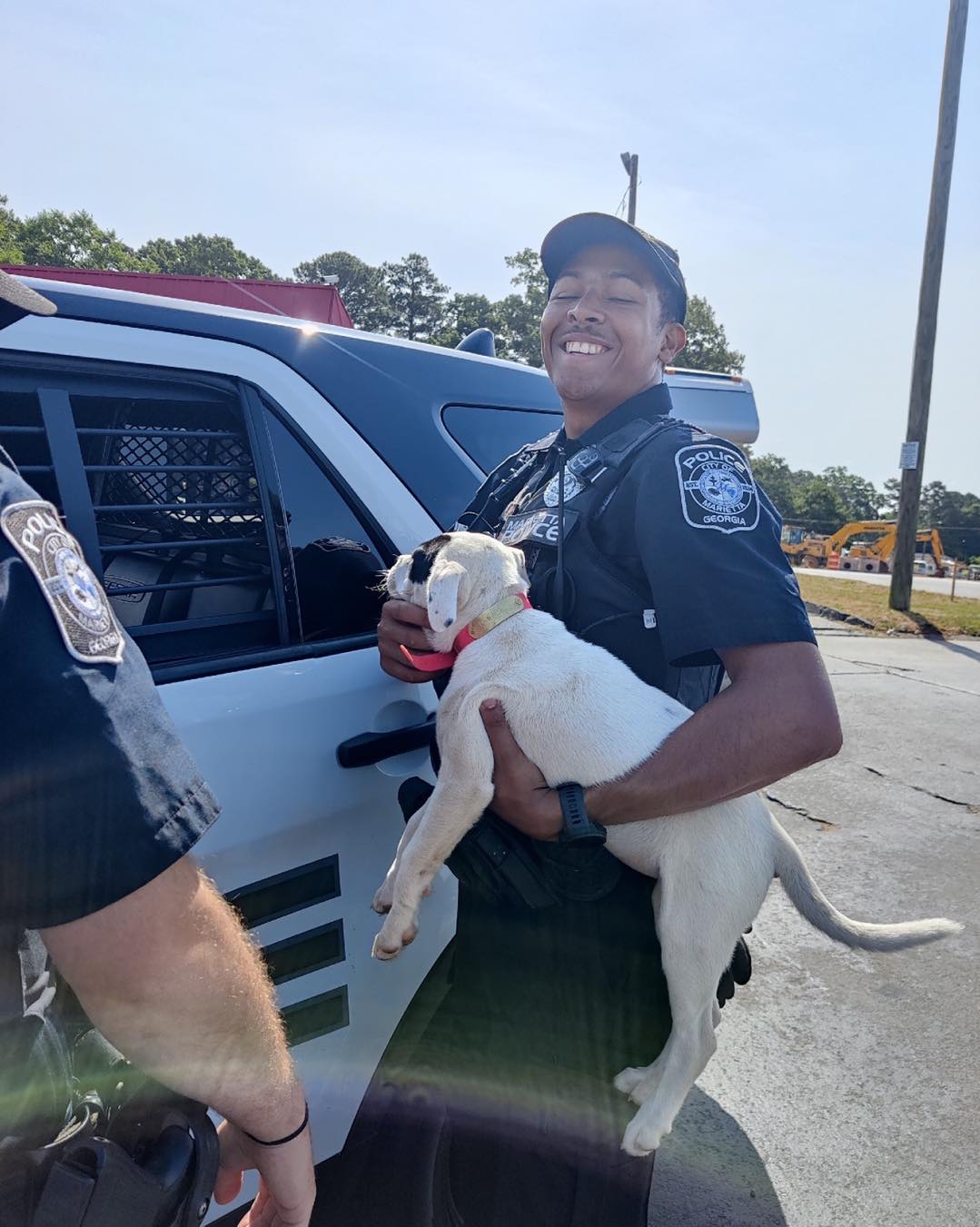 officer-holding-a-puppy-and-standing-next-to-a-police-car officer holding a puppy and standing next to a police car